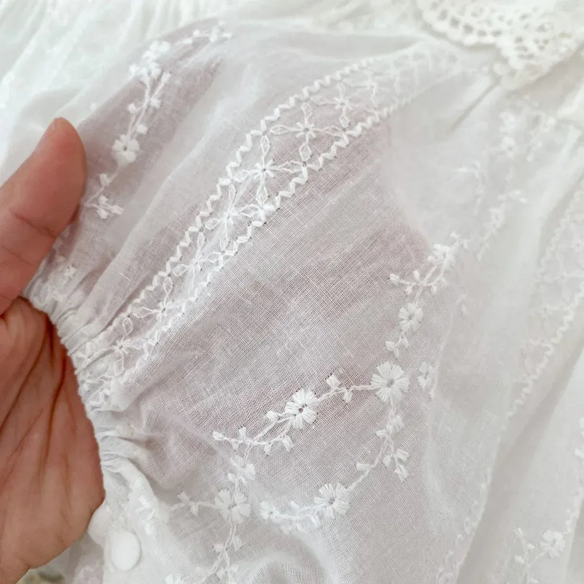 ホワイトの半袖レース刺繍、花柄モチーフの縁取りが見える