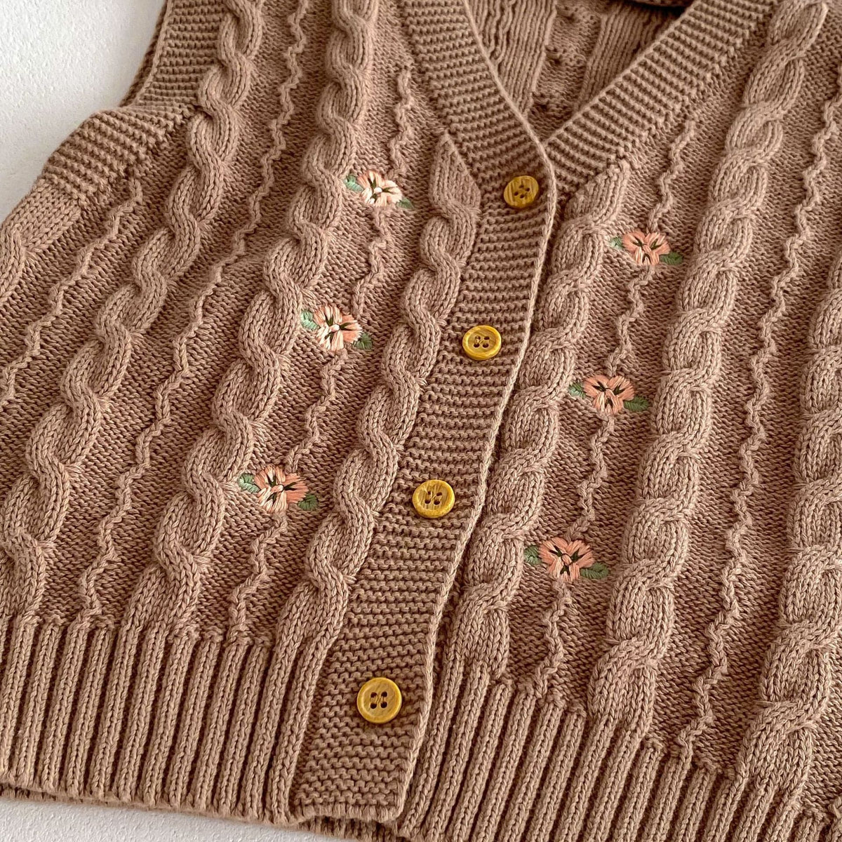 キャメルのニットベスト前面アップ、花刺繍とゴールドのボタンが並ぶ