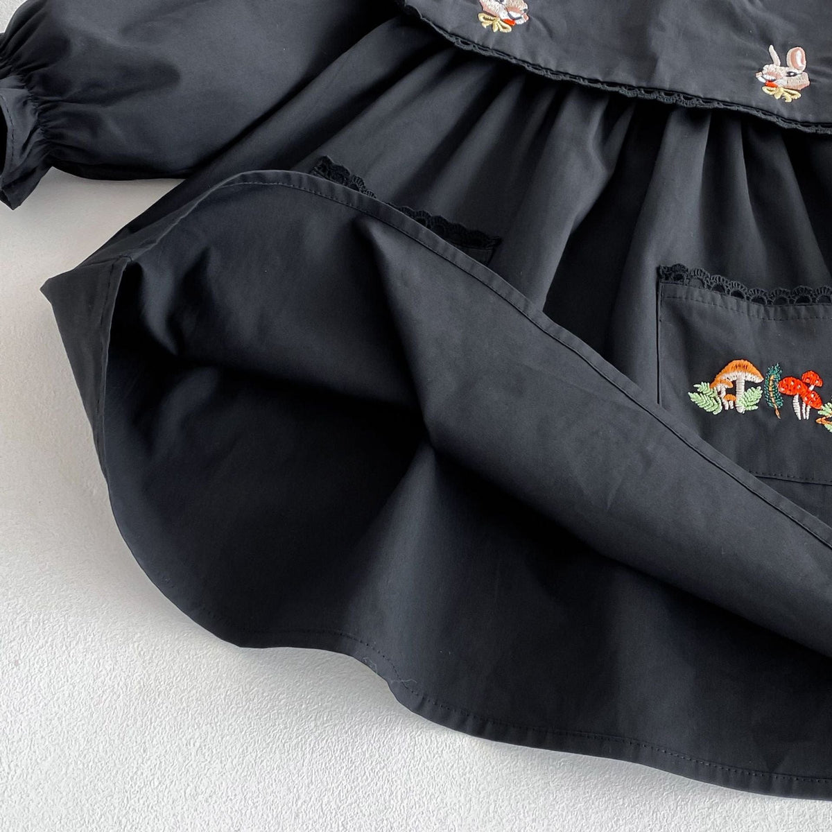 黒の長袖ワンピース、前ポケットの刺繍と丸みのあるギャザーデザイン