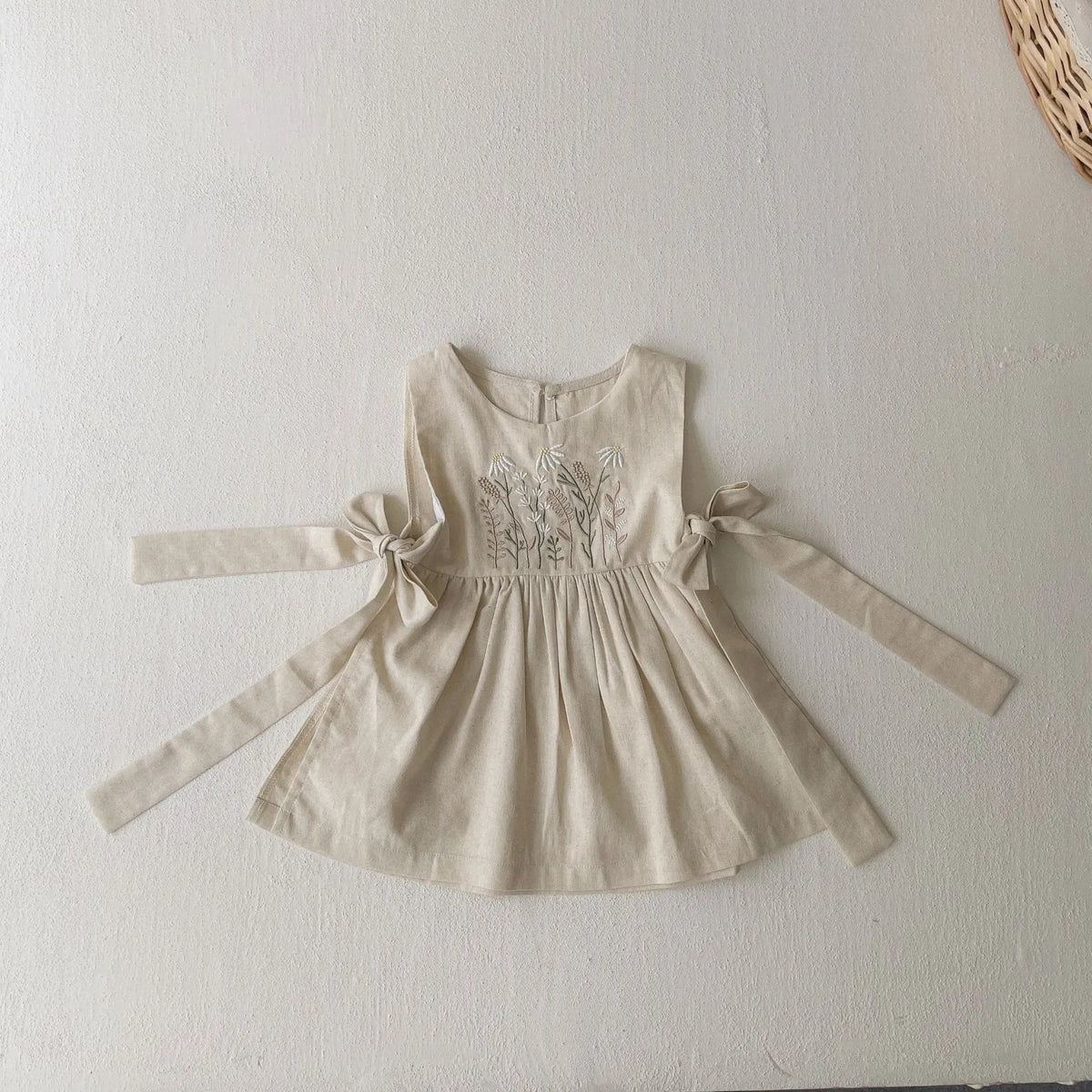 生成り色のベビー用ノースリーブワンピース、花柄刺繍と左右リボンの立体シルエット