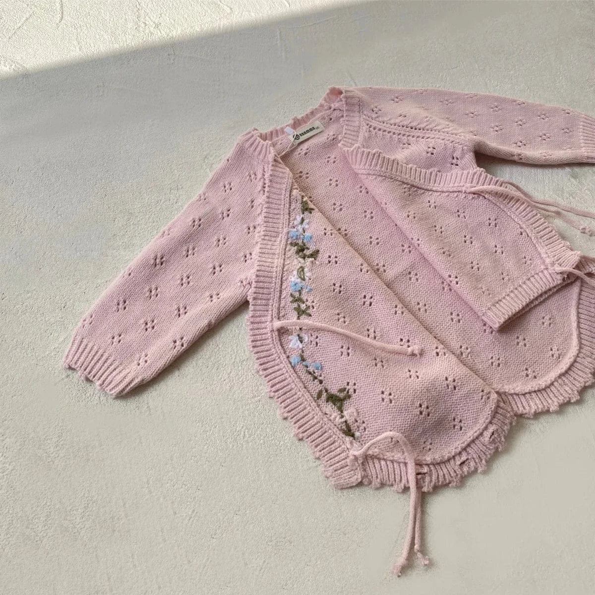 ピンクの長袖ニットボディスーツ、花刺繍とフリル前立て、キャップ付き