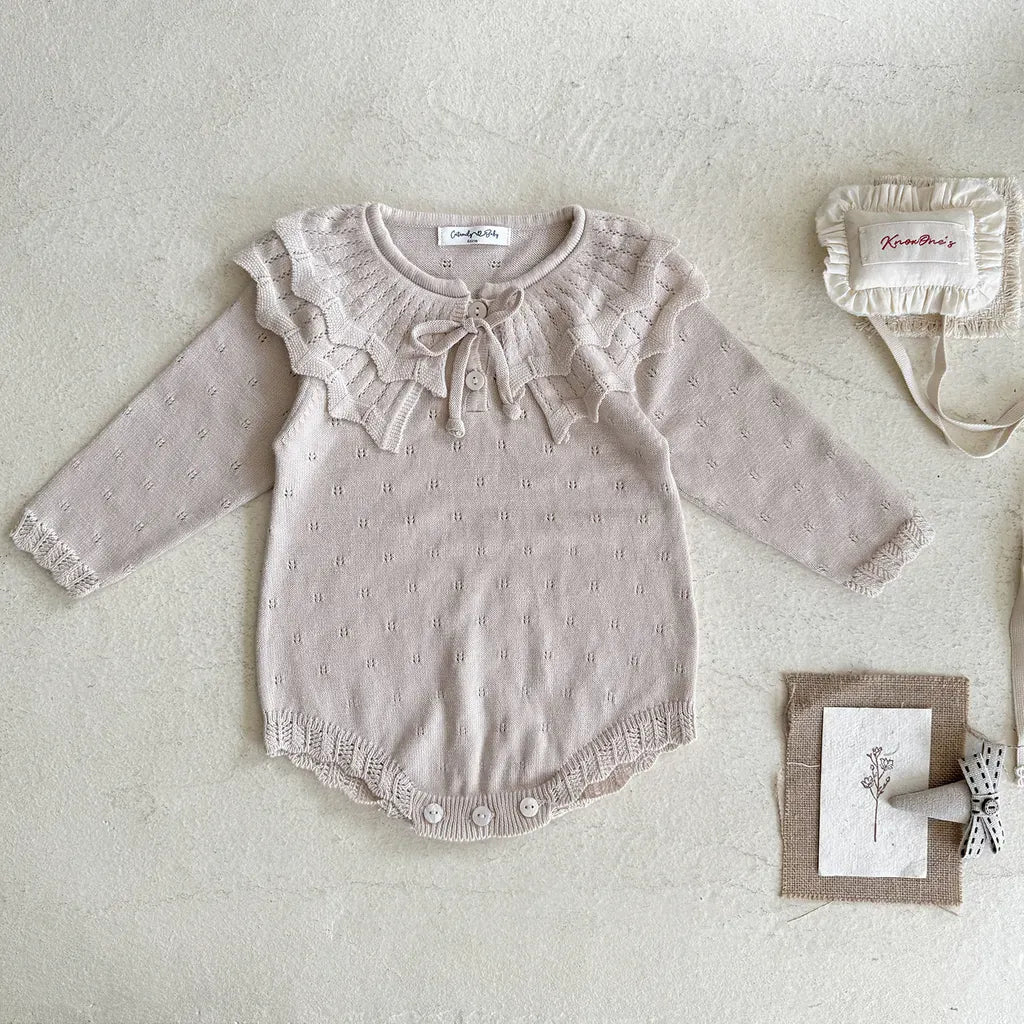 薄いピンクのニットロンパース、フリル襟とリボン付きの前面デザイン