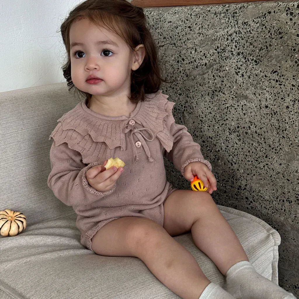 ピンクのフリル襟リボン付き長袖ニットロンパースを着た子ども