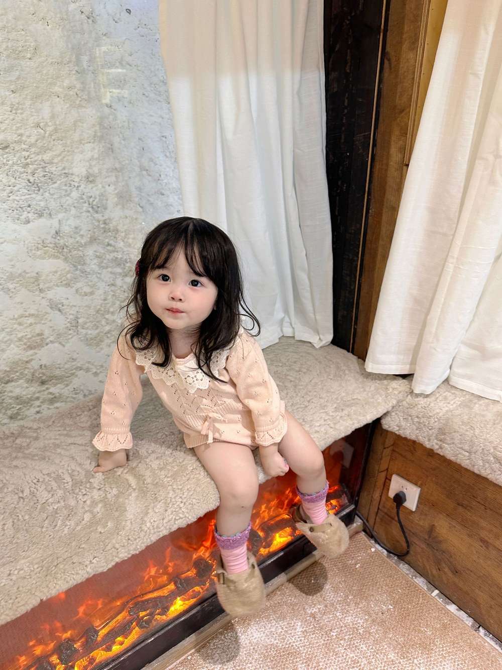 ピンクの長袖ニットロンパース(レースフリル襟)を着たベビー
