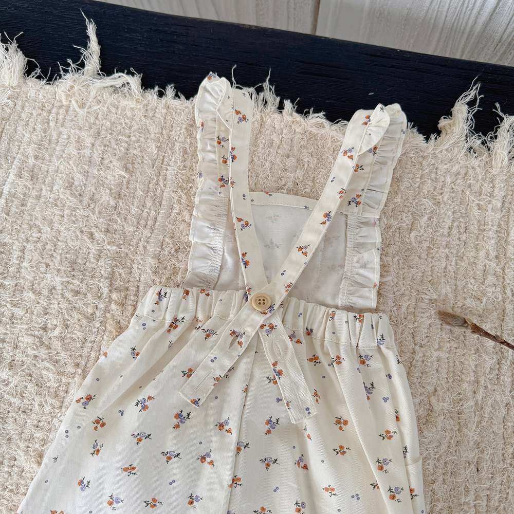 小花柄の白いサロペットパンツ、フリルの肩ひもと胸元ボタン付き