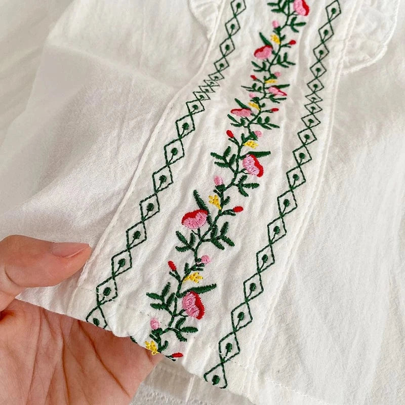 白ブラウスの刺繍アップ。赤・緑の花と縁取り模様の縦ライン