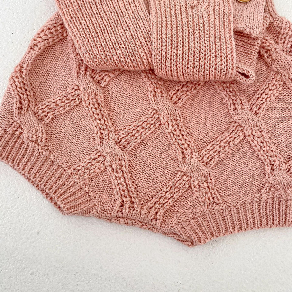 パールピンクのニットロンパース、ハート風の透かし編みと裾の立体リブ