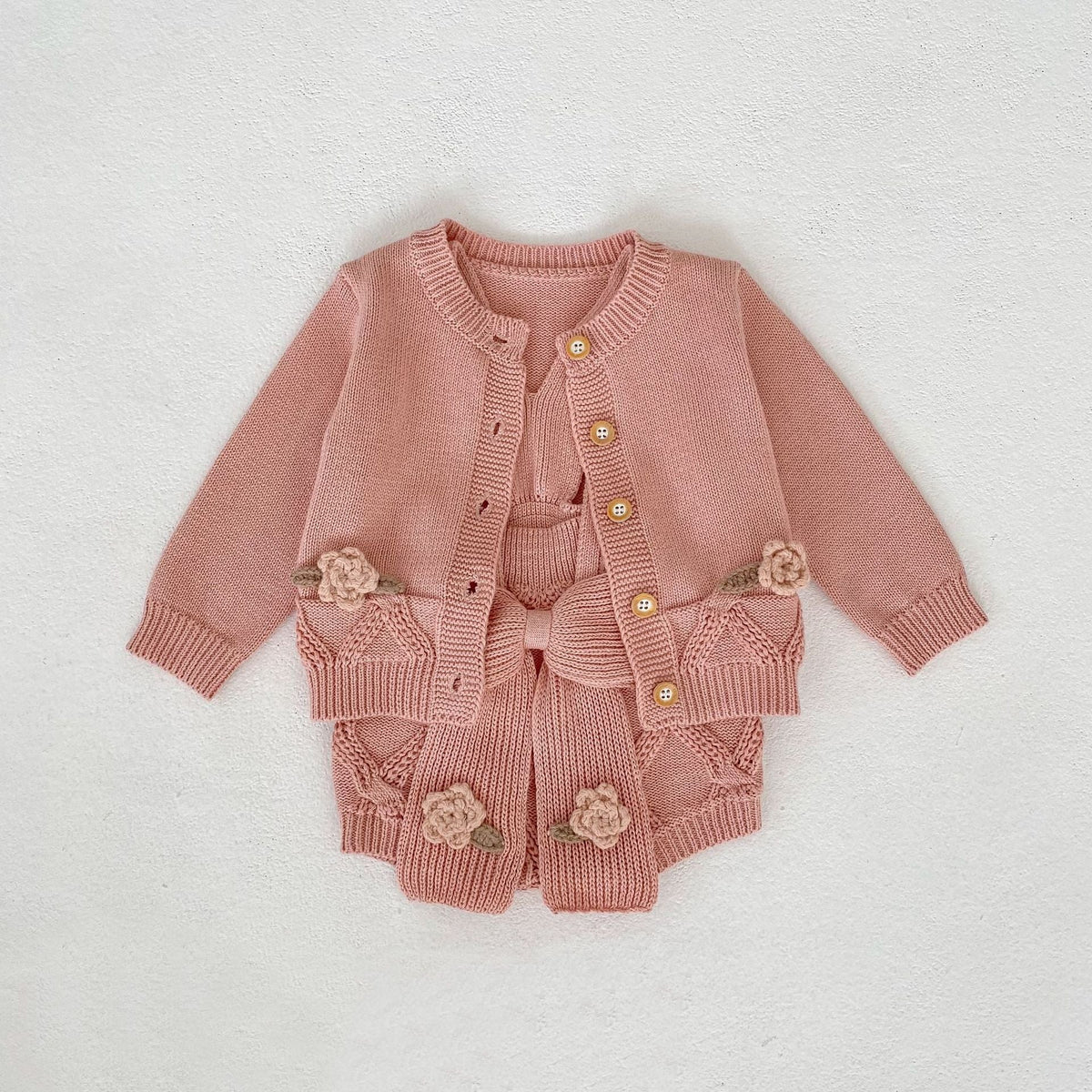 パールピンクのニットカーディガンとロンパース。フロントボタンと花の刺繍