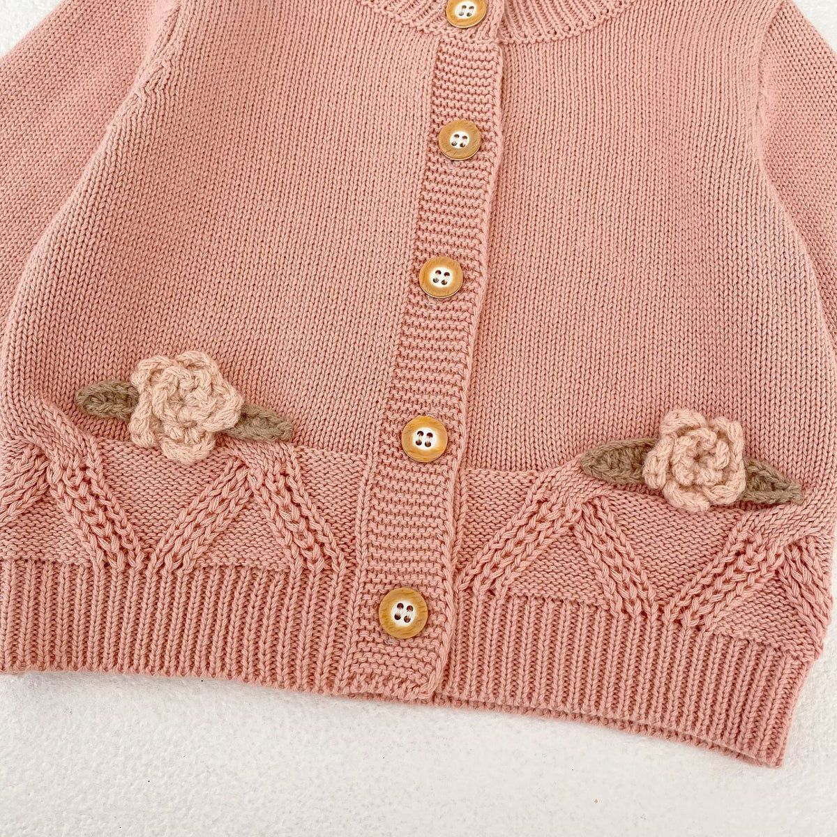 パールピンクのニットカーディガン裾。花刺繍と前開きボタン列のアップ