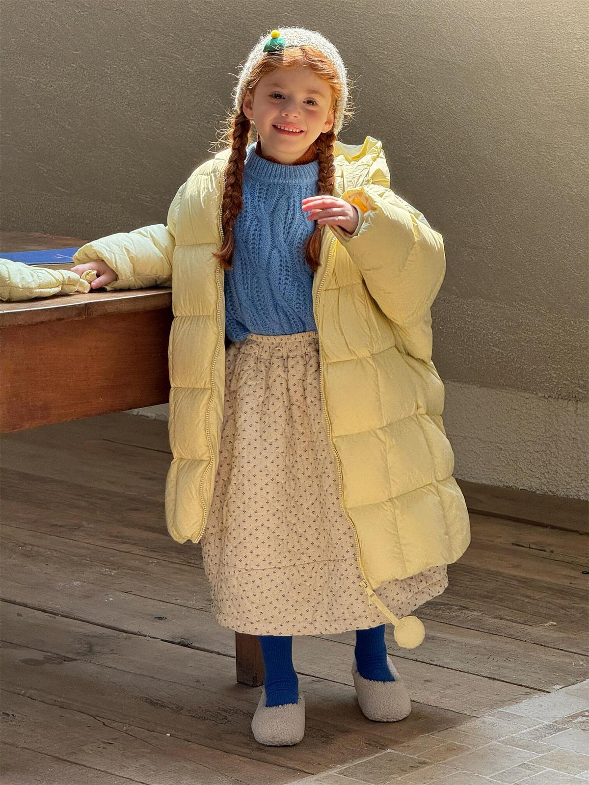 イエローダウンコートの子ども、青いニットとスカートが見える