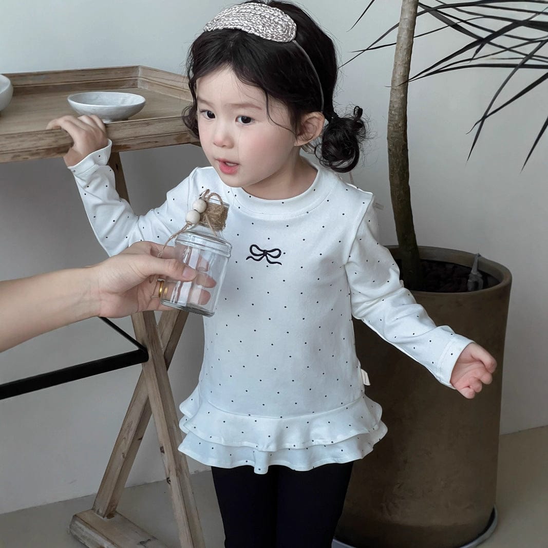 白のドット柄長袖Tシャツ裾フリル(リボンモチーフ)と黒フレアロングパンツ