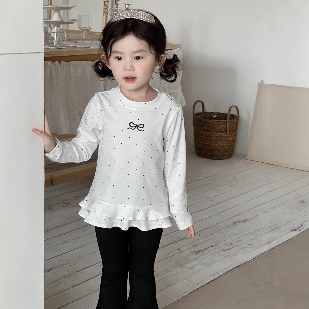 白ドット柄長袖Tシャツ(裾フリル、リボン刺しゅう)と黒フレアパンツ