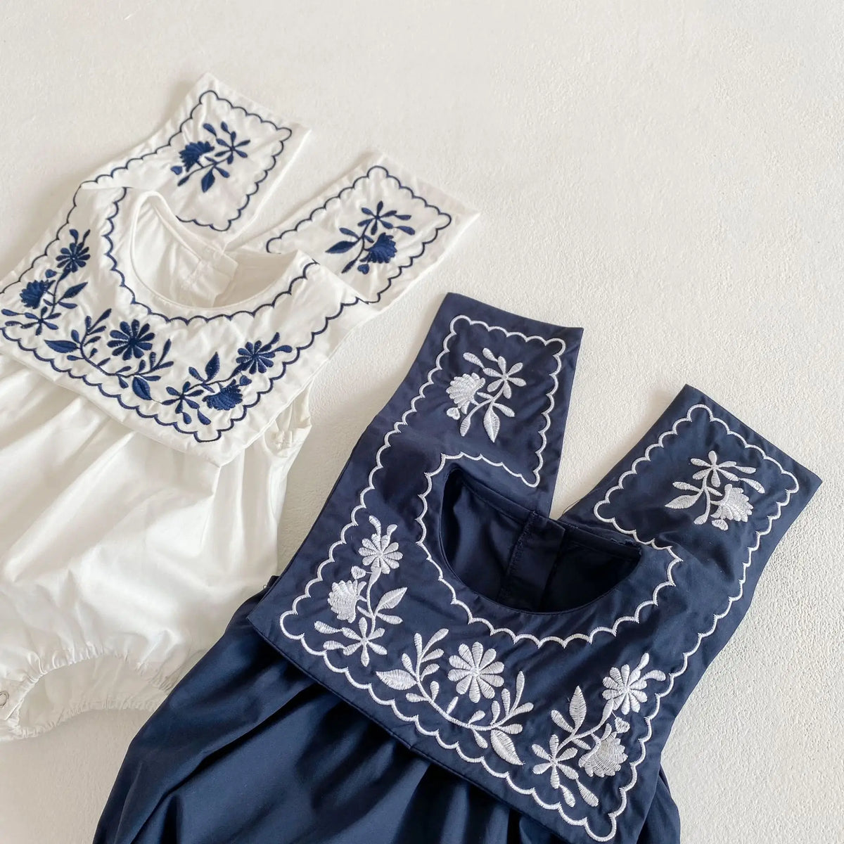 フラワー刺繍の襟と前立てが特徴の白・濃紺ノースリーブボディスーツ