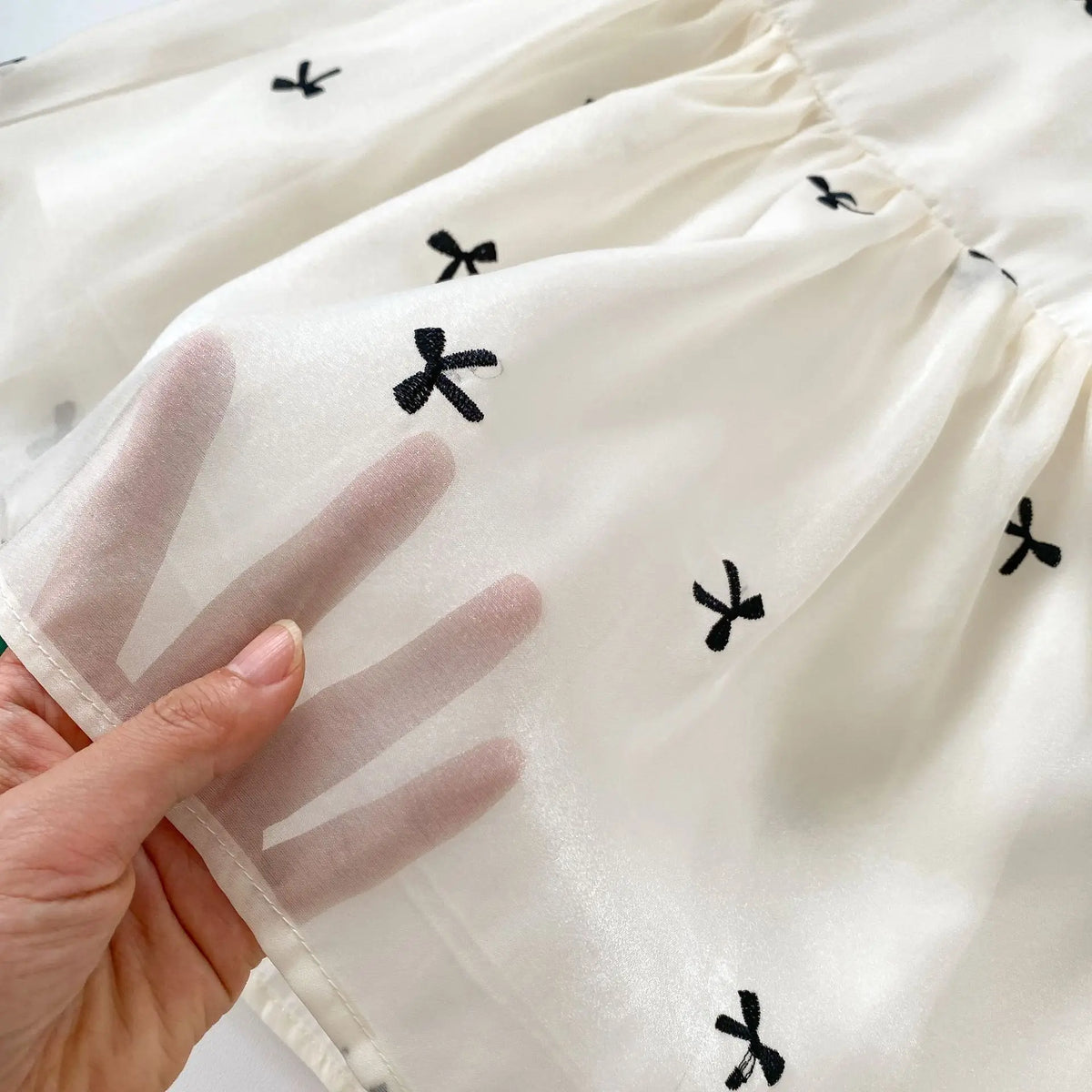 白いベビー半袖ドレスのアップ、黒い小さなリボン模様とやわらかな生地