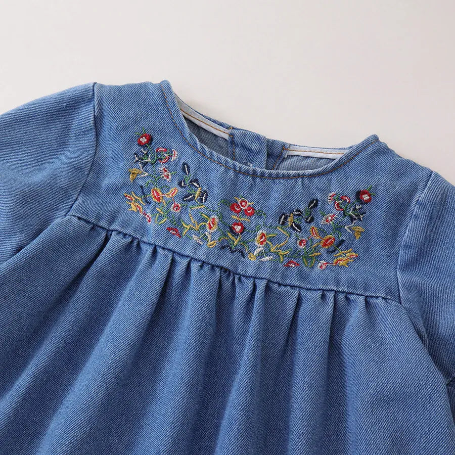 青いデニムワンピース、胸元のカラフル花刺繍とギャザーフリル