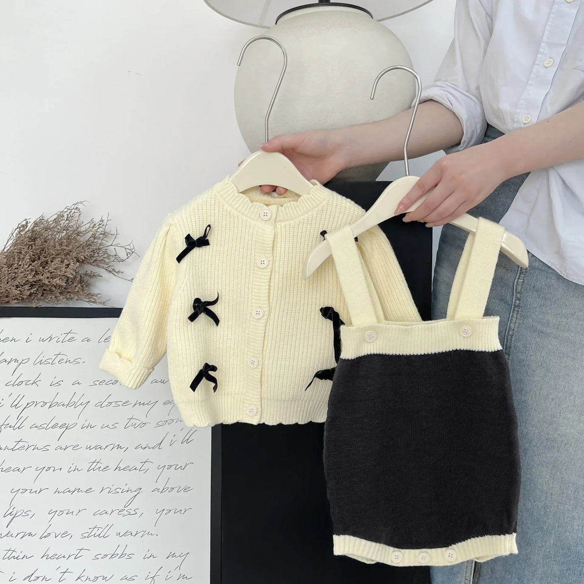 吊りデザインのバイカラーボディスーツとクリームカーディガン。黒リボン刺繍、前面。