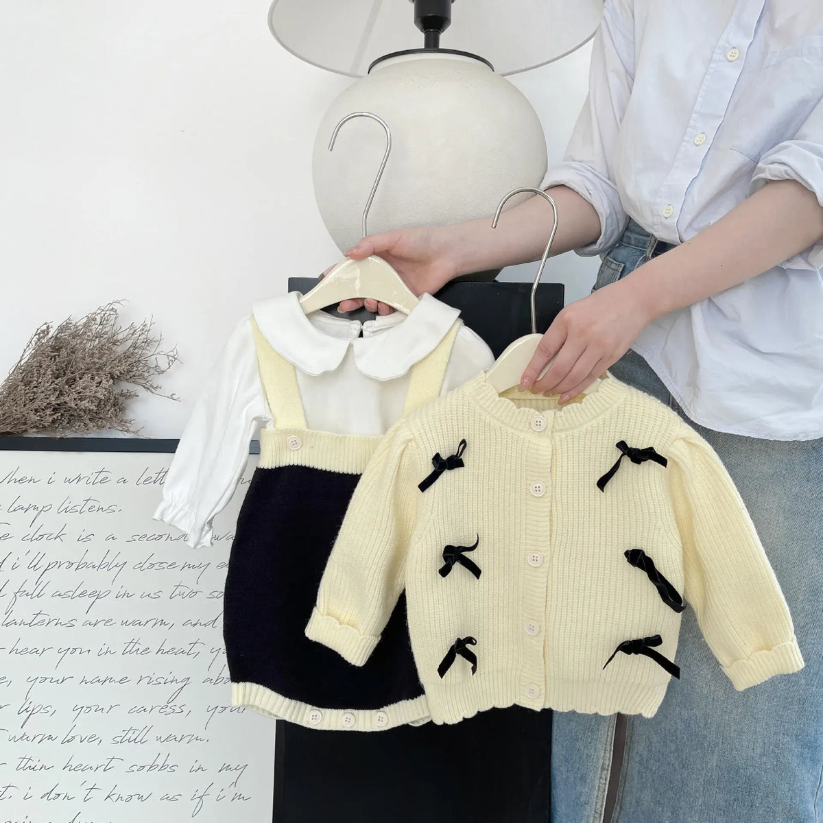 ベビー服。クリームのニットカーディガン(ボタン)と黒のサスペンダーボディスーツ(吊り)。