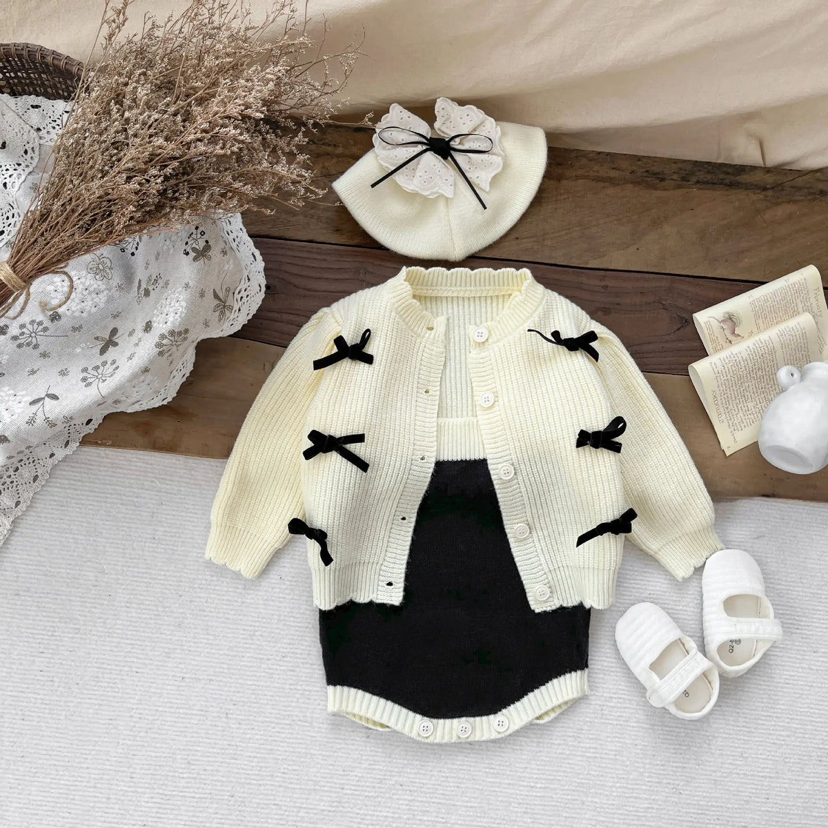 リボン刺繍のクリーム色ニットカーディガンと黒のサスペンダーボディスーツ(前面)。