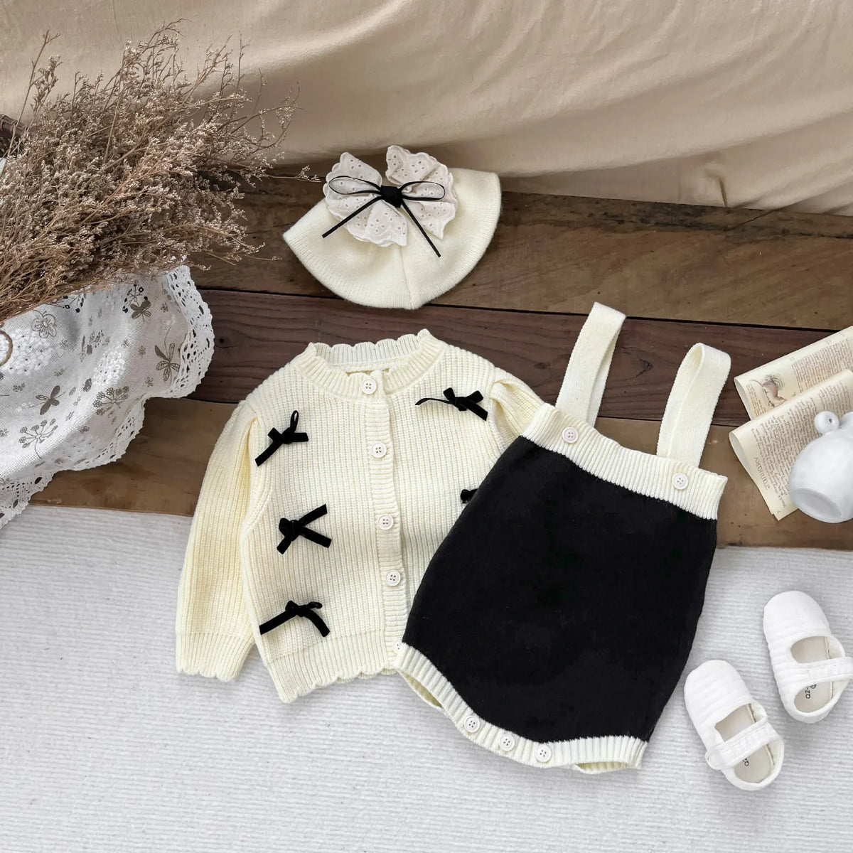 ベビー用ニットカーディガンとサスペンダーボディスーツセット。クリーム×黒、リボン刺繍付き。