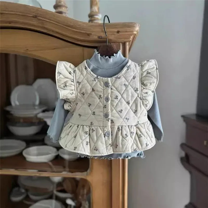 キルティング風素材のフリル付きベビー服、白系ボディと長袖のセットアップ