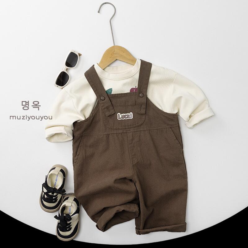 ダークブラウンのサロペット風と生成り長袖Tシャツ、前面にフード風プリント