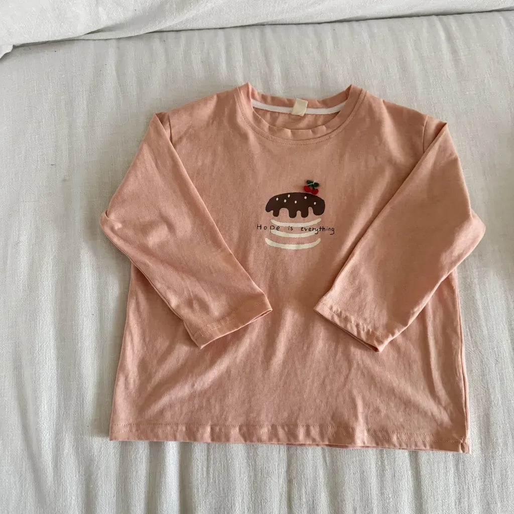 ピンク系の長袖Tシャツ、胸にケーキ柄のくま刺繍