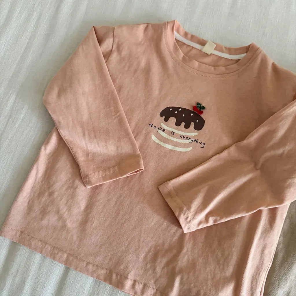 アプリコット系の長袖Tシャツ、胸元の刺繍デザインが入ったクルーネック