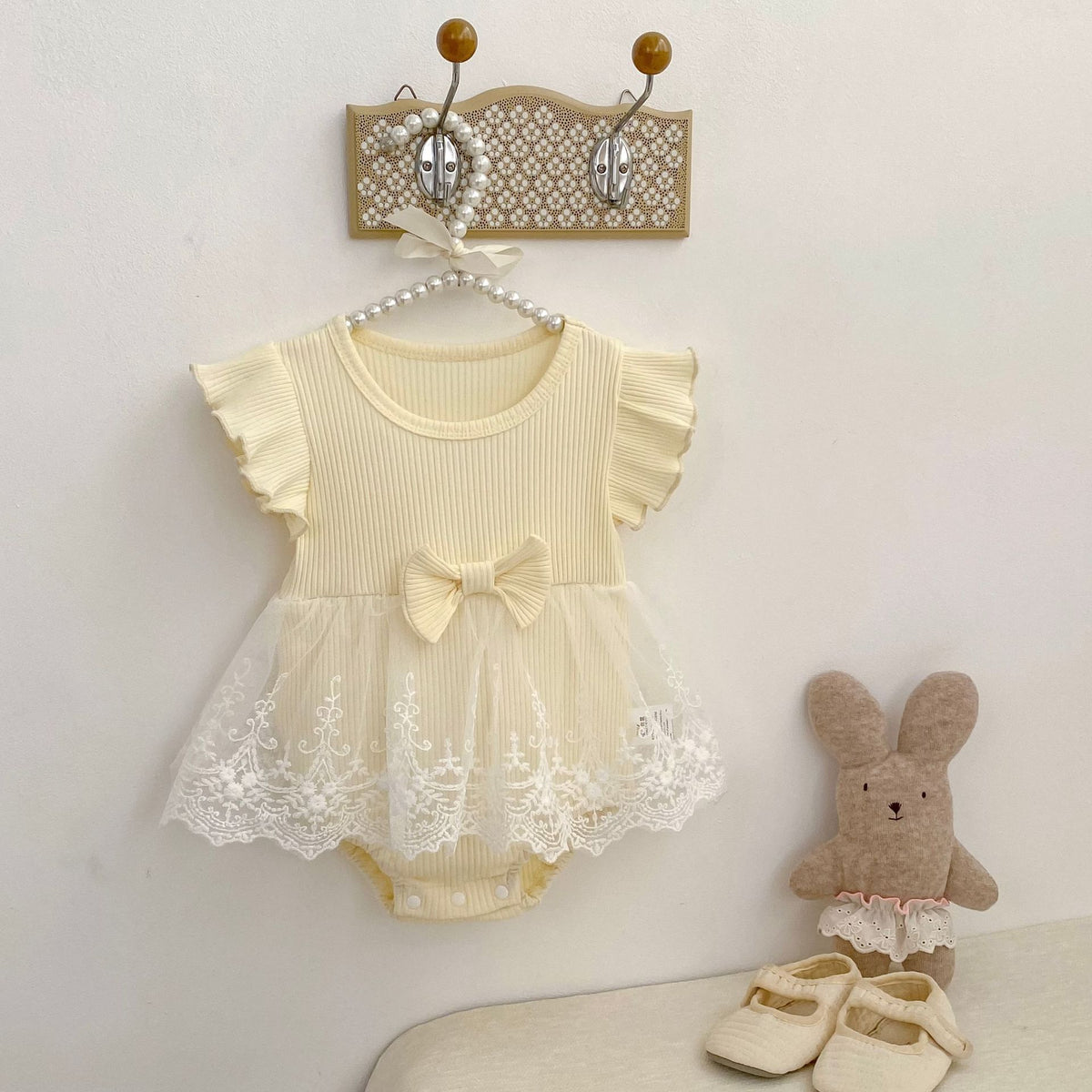 クリーム色のベビー用ロンパース、フリル袖と胸元リボン、レースチュールスカート