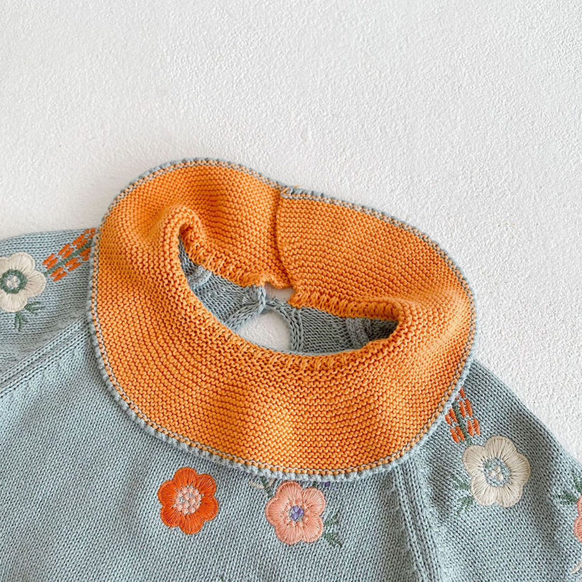 ベビーニットのオレンジ配色フリル襟。ライトブルー地に花の刺繍