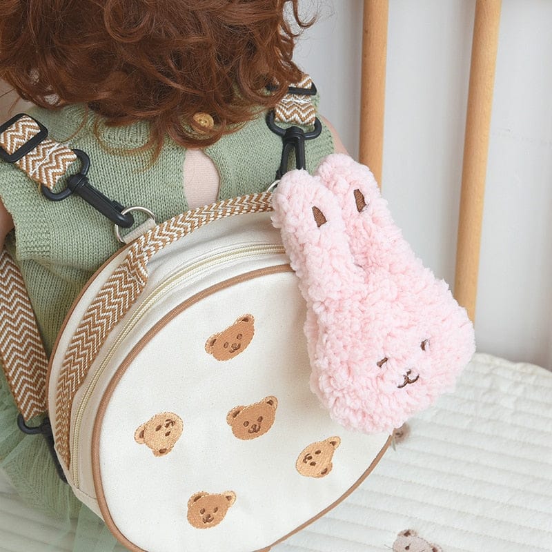 丸型ベビーリュック、くま刺繍白地。ピンクのふわふわぬいぐるみチャーム付き。