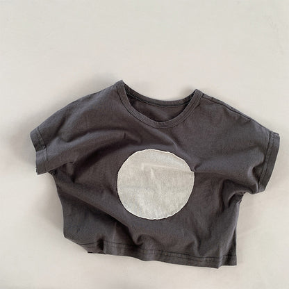 ダークグレーのキッズ半袖Tシャツ、白い丸パッチのフロントデザイン