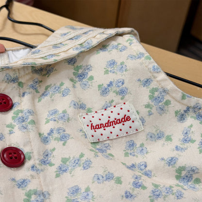 ベージュ花柄サロペットのアップ、刺繍ラベルと赤いボタンが見える