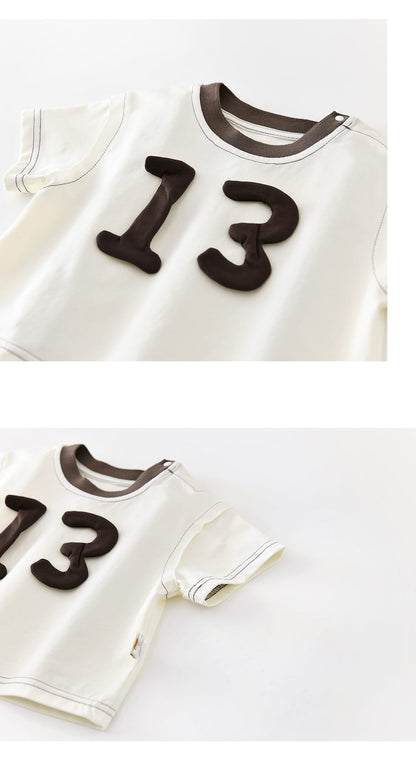 白い半袖Tシャツの前面アップ。立体パッチの数字13とブラウンの丸首リブ
