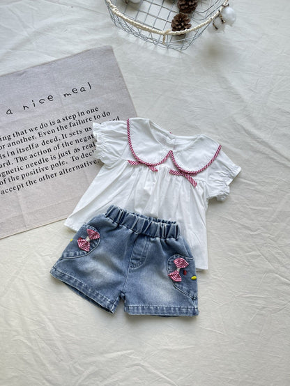 白いブラウスと青いデニムショートパンツ、赤パイピング衿と刺繍ワッペン