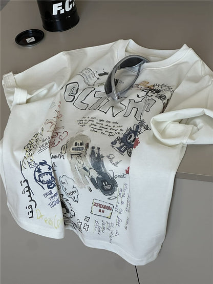 クリーム色の半袖Tシャツ、ロゴ風落書きとモンスター風キャラのプリント