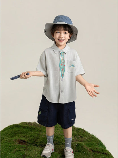 生成り色の半袖シャツ、ネクタイ風プリント入り。前立てボタンと胸ポケット