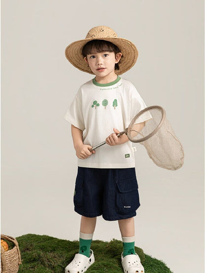 ベージュ半袖Tシャツと紺デニム半ズボン。葉柄プリントとフラップポケットが特徴