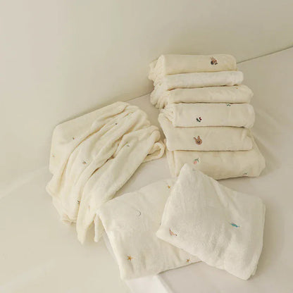 ベビーブランケット クリーム色、折り重ねたフリース毛布。刺繍の動物柄と星・月