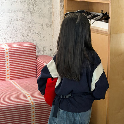 背面の紺色長袖Tシャツ、ベージュ切替パネルと赤い差し色が見える