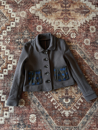 ダークグレーのジャケット、前ボタン留めと青いパッチデザインのポケット